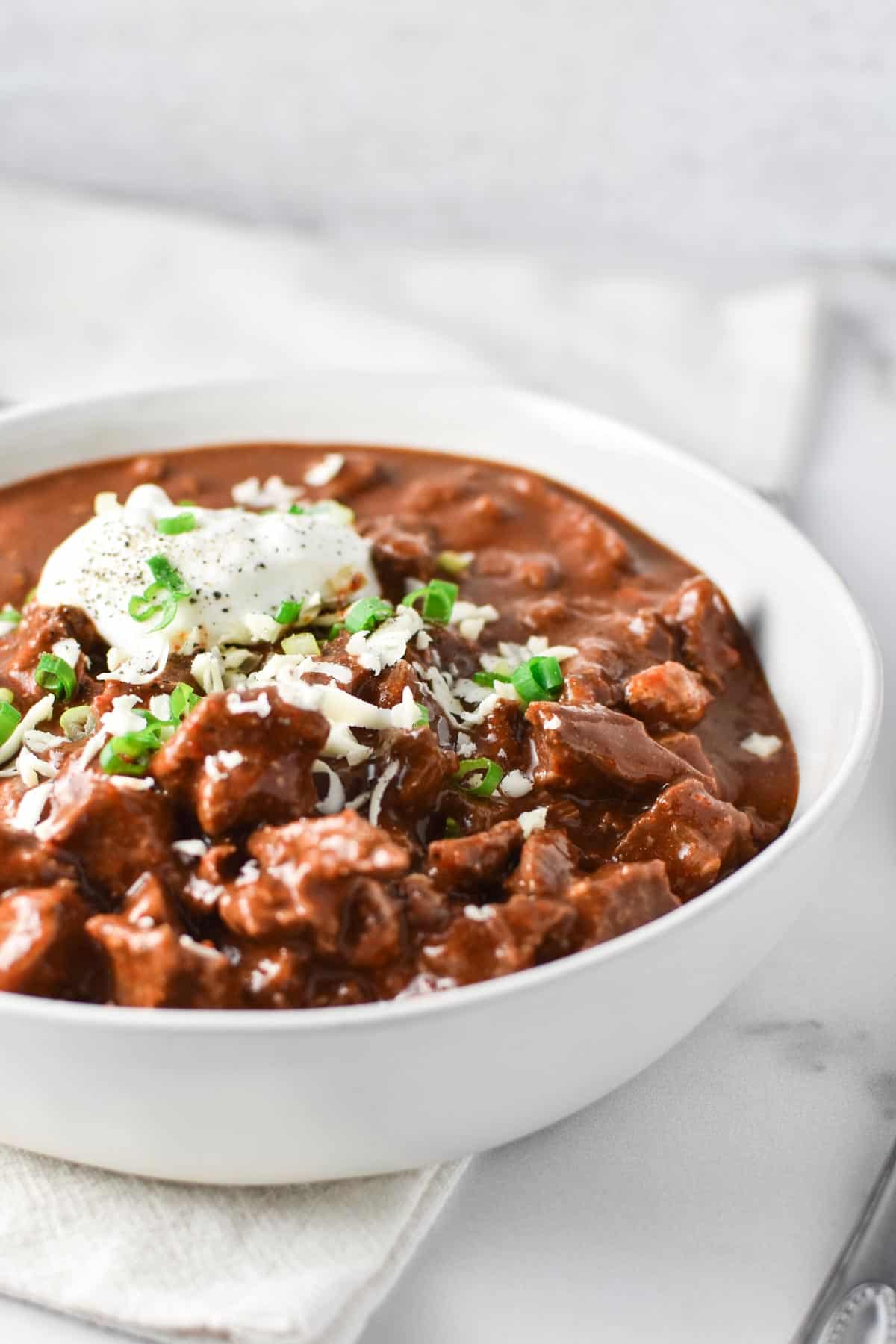 A bowl of thick beef chili topped with sour cream and green onions.