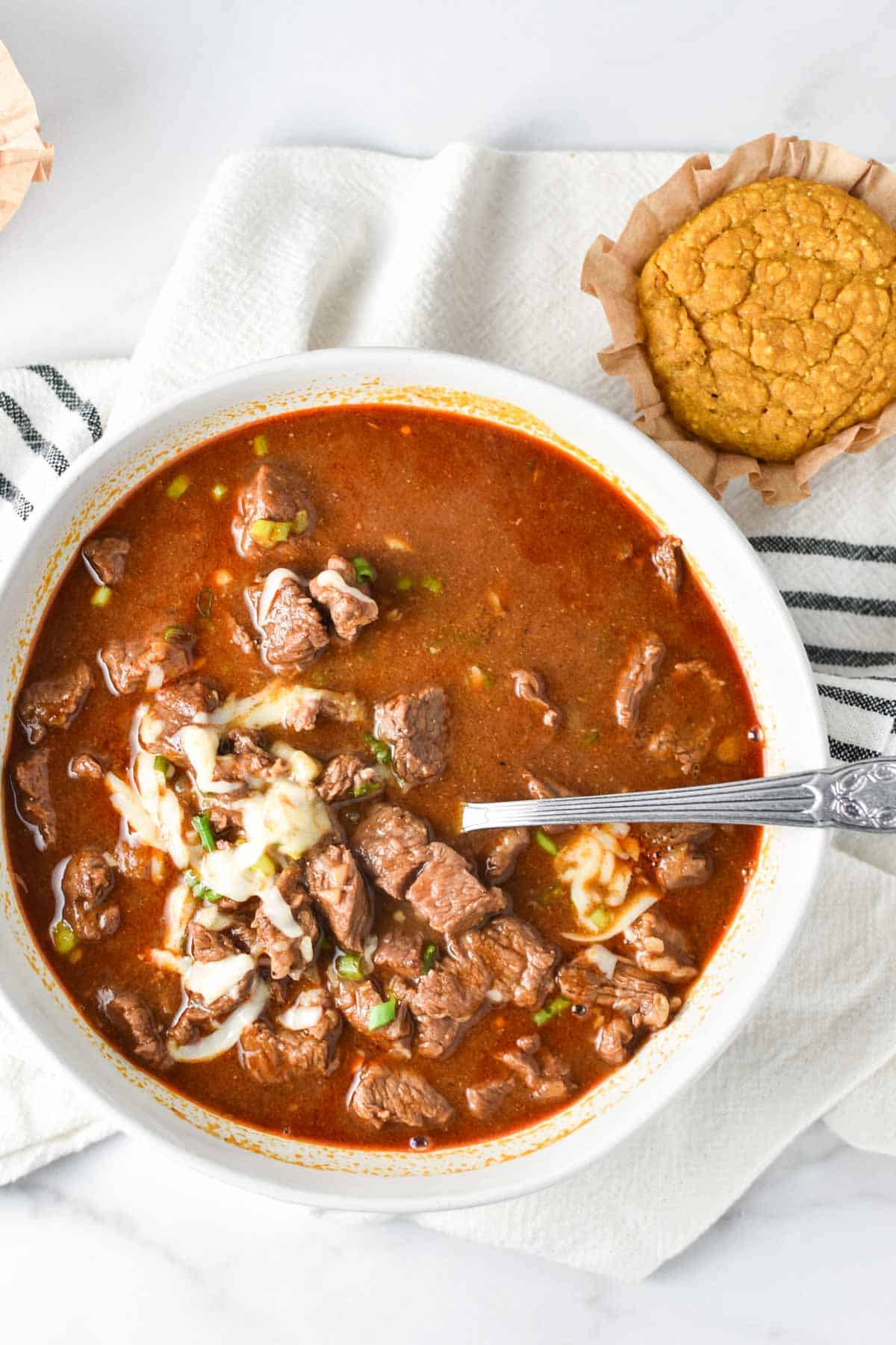 A white bowl with chili and melted cheese on top.