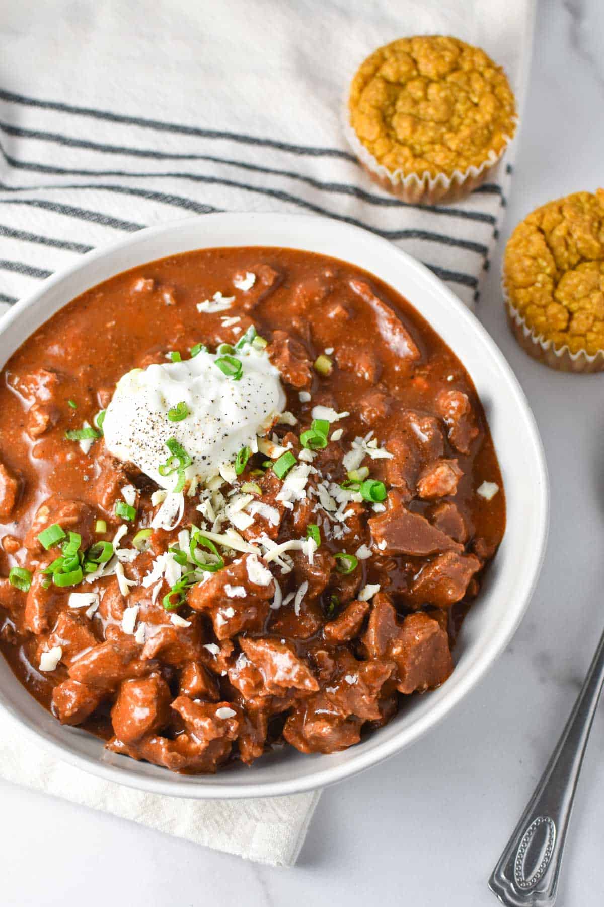 A thick bowl of chili with two cornbread muffins and a striped towel.