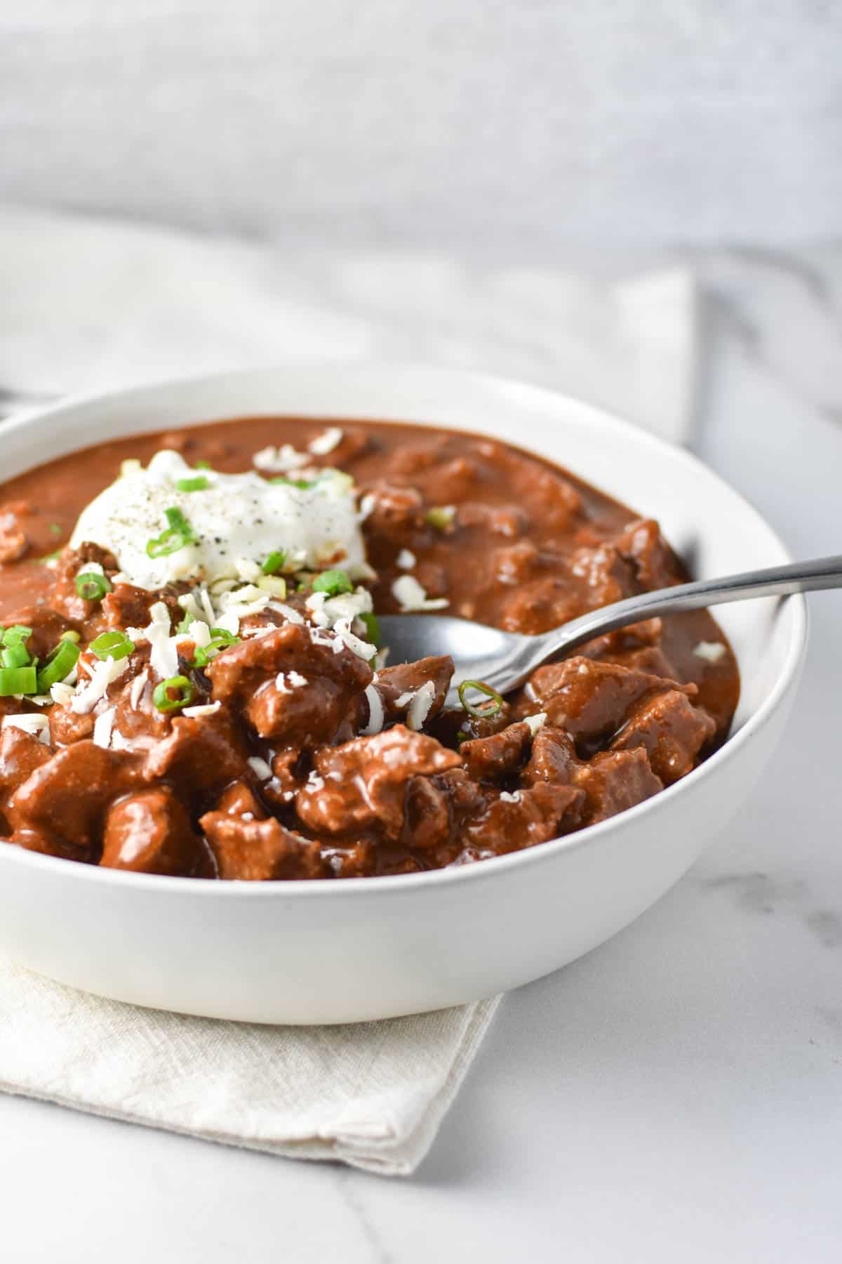 A spoon dipping into a bowl of chili without tomatoes or beans.