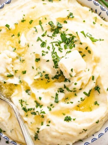 A blue and white bowl filled with fluffy mashed Boursin Potatoes topped with chives and melted butter.