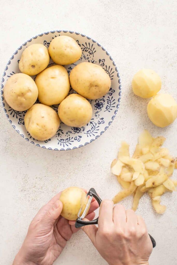 A hand peeling Yukon gold potatoes.