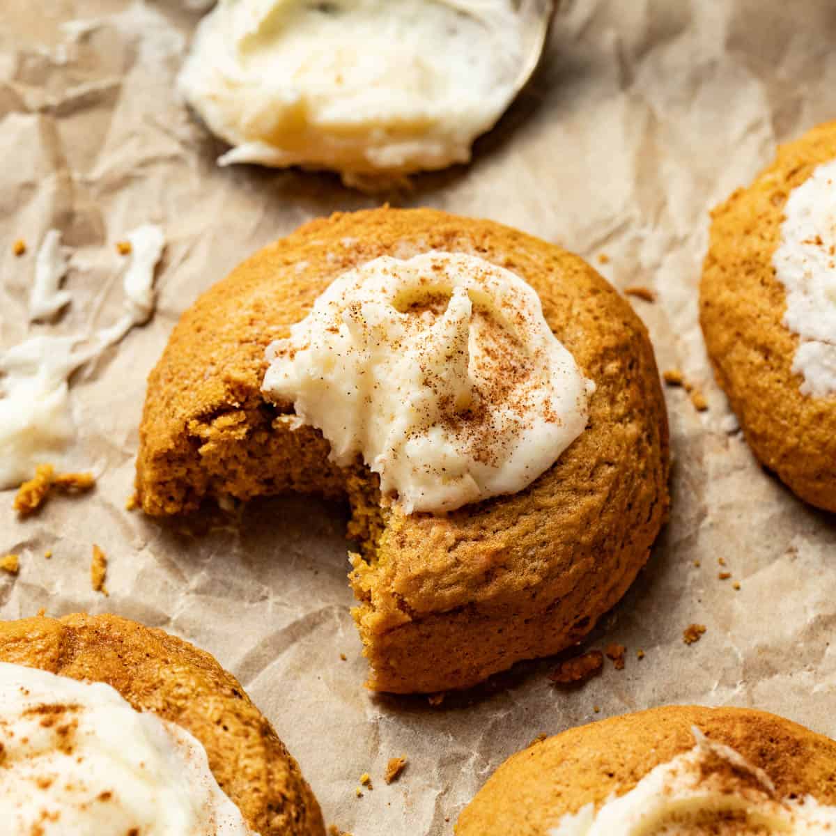 A pumpkin cookie with cream cheese frosting and cinnamon with a bite out of it.