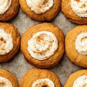 A baking sheet with pumpkin cookies topped with cream cheese frosting and cinnamon.