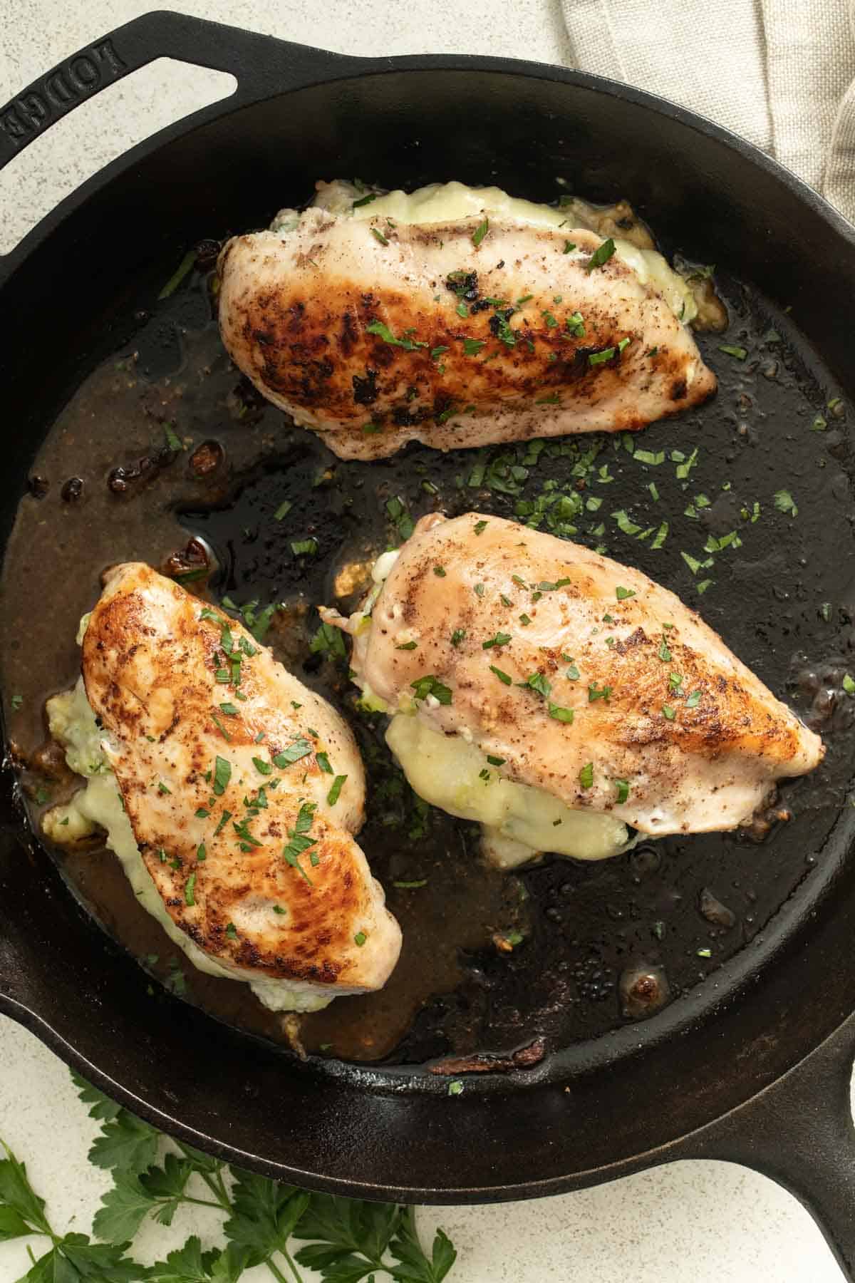 Three stuffed chicken breasts being seared in a cast iron pan.