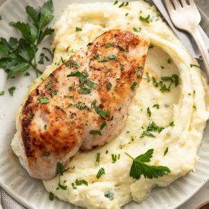 Ricotta stuffed chicken on top of mashed potatoes with parsley.