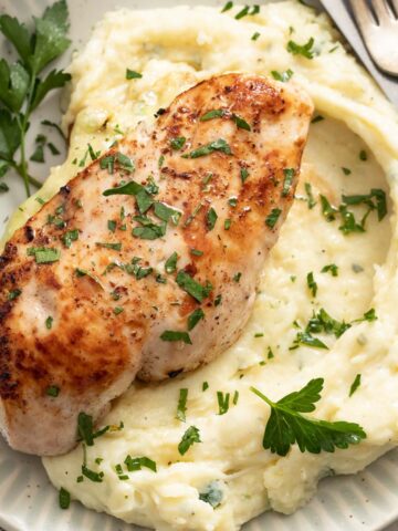 Ricotta stuffed chicken on top of mashed potatoes with parsley.