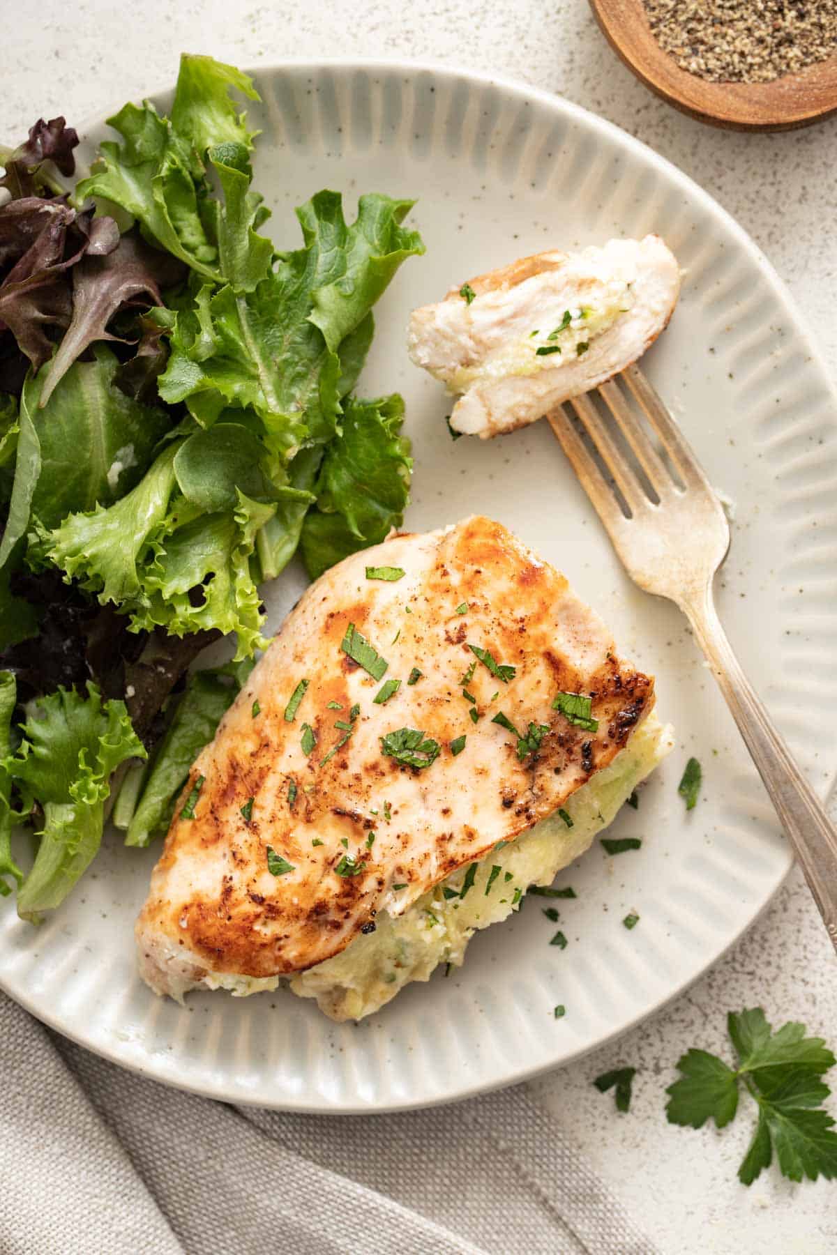 A sliced stuffed chicken with a fork, next to mixed greens.