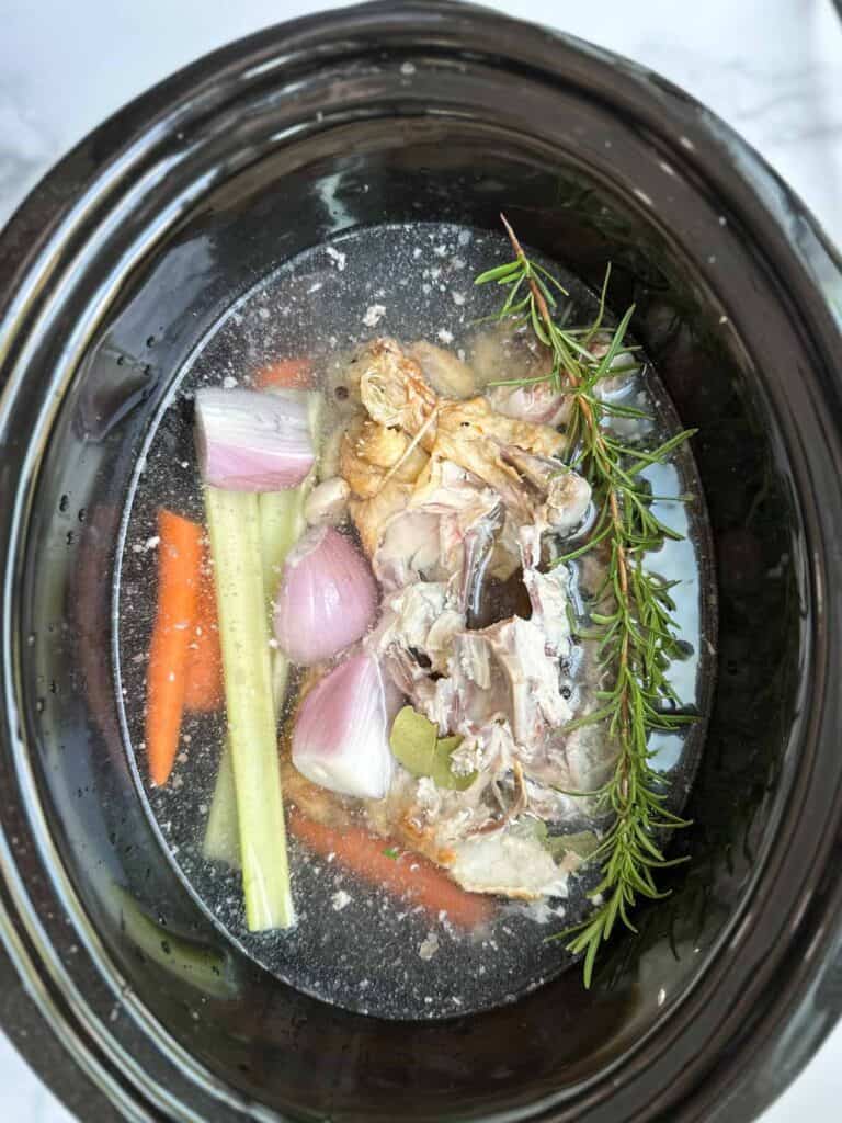 Ingredients for chicken broth in a crockpot with water.