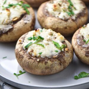 Baked mushrooms stuffed with Boursin cheese topped with parsley on a gray plate.