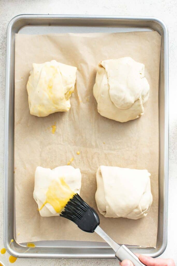 Brushing puff pastry pockets with egg to secure them.