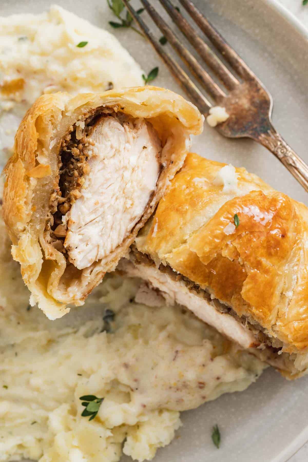 Sliced chicken wellington to show the mushroom duxelle and dijon coating on the chicken breast inside the puff pastry.