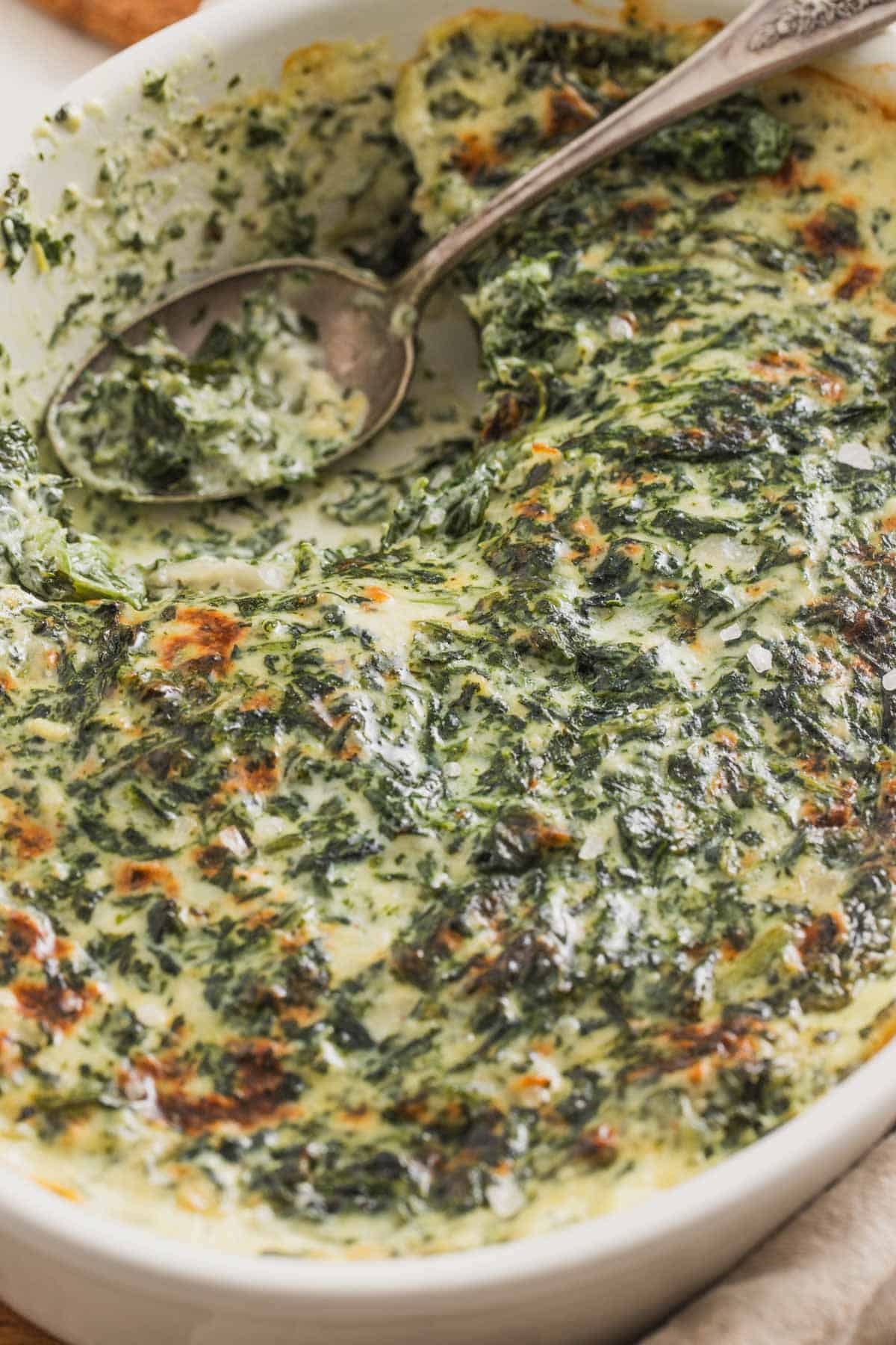 A casserole dish of baked creamed spinach with melted cheese on top.