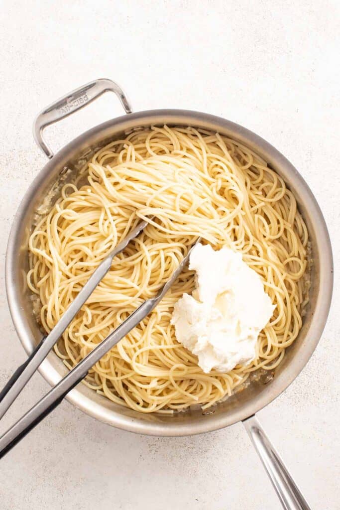 Pasta in a saucepan with mascarpone cheese added to it.