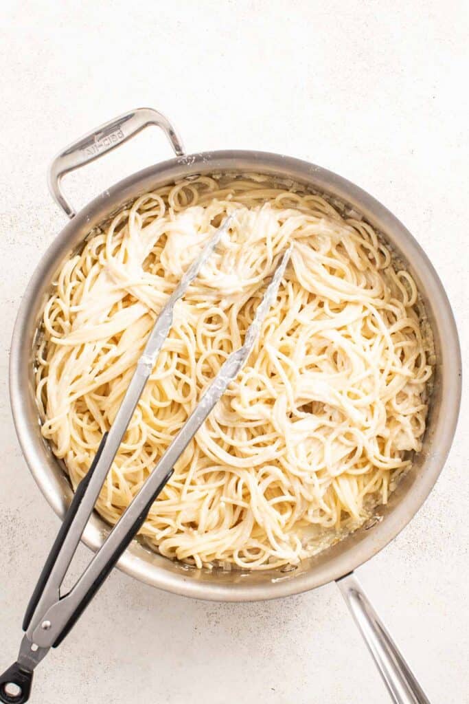 Tongs mixing mascarpone cheese into pasta.