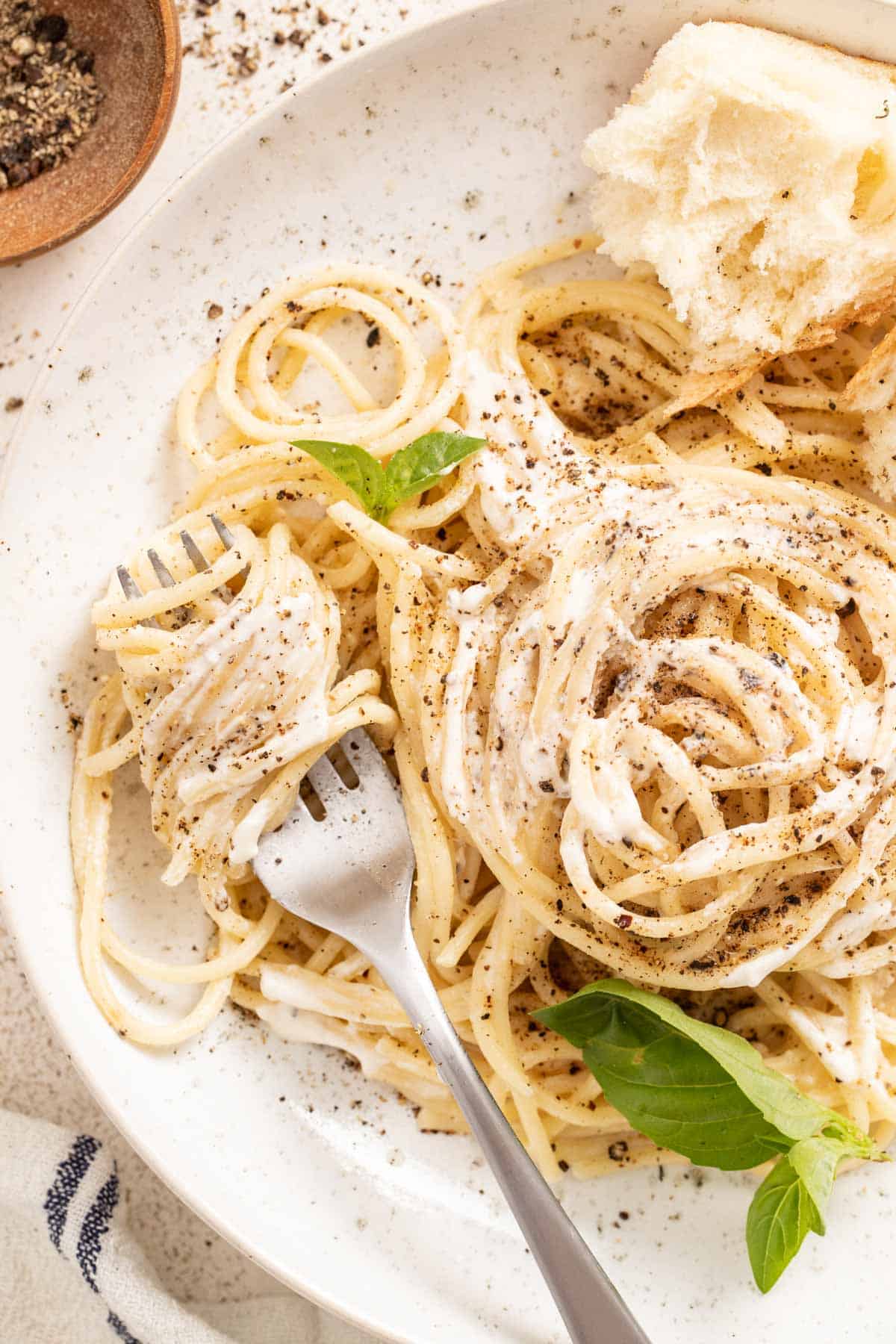 Creamy pasta twirled around a fork next to a slice of bread and fresh basil.