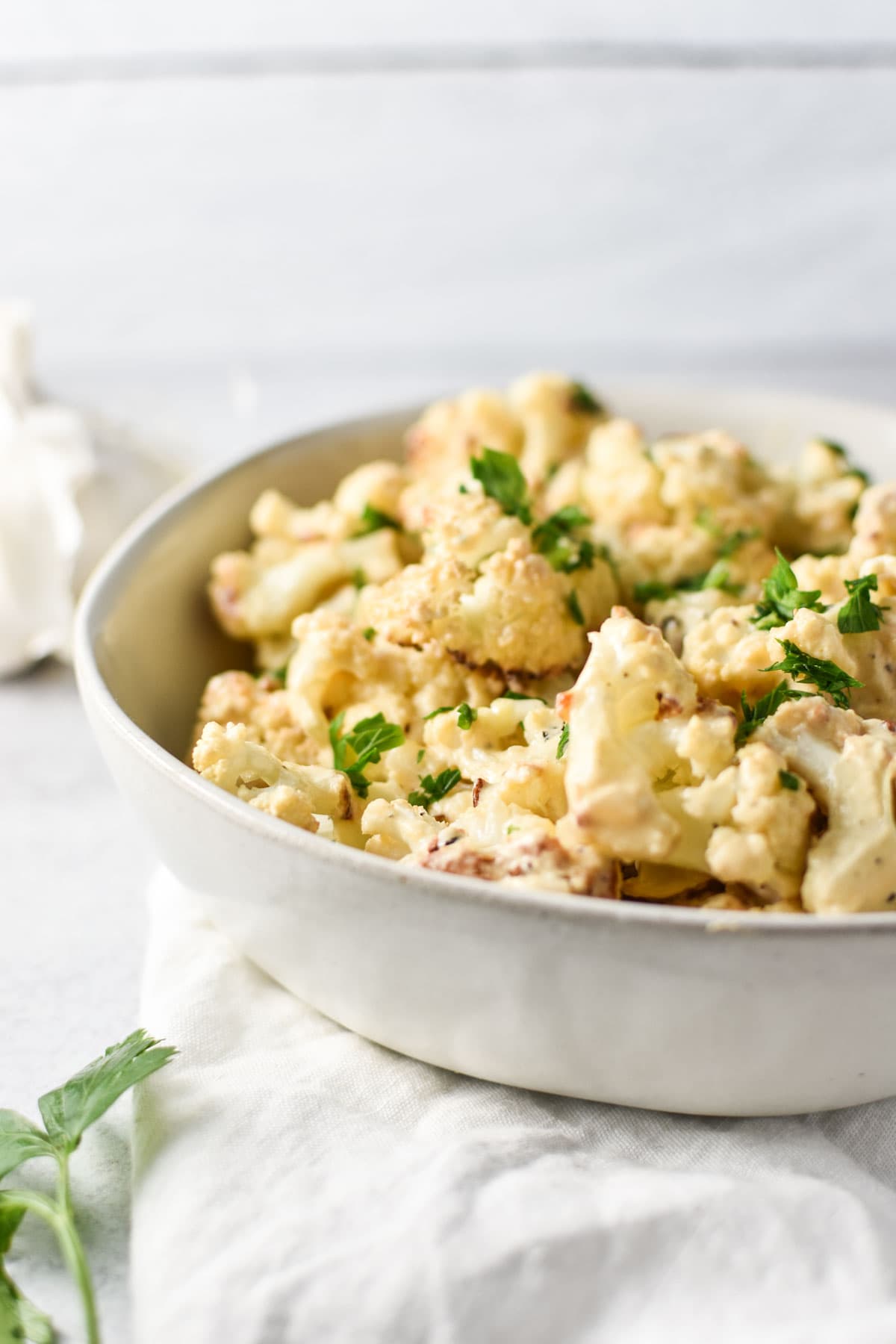 A bowl of cheesy roasted cauliflower topped with parsley.