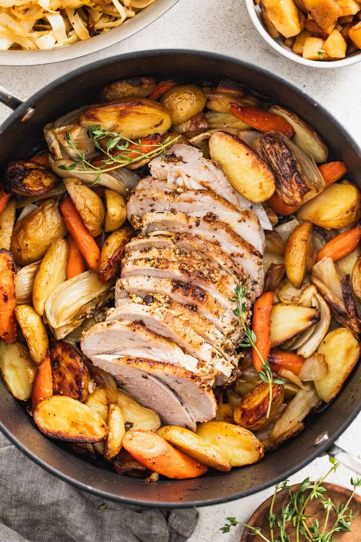 Sliced pork roast in a dutch oven surrounded by root vegetables.