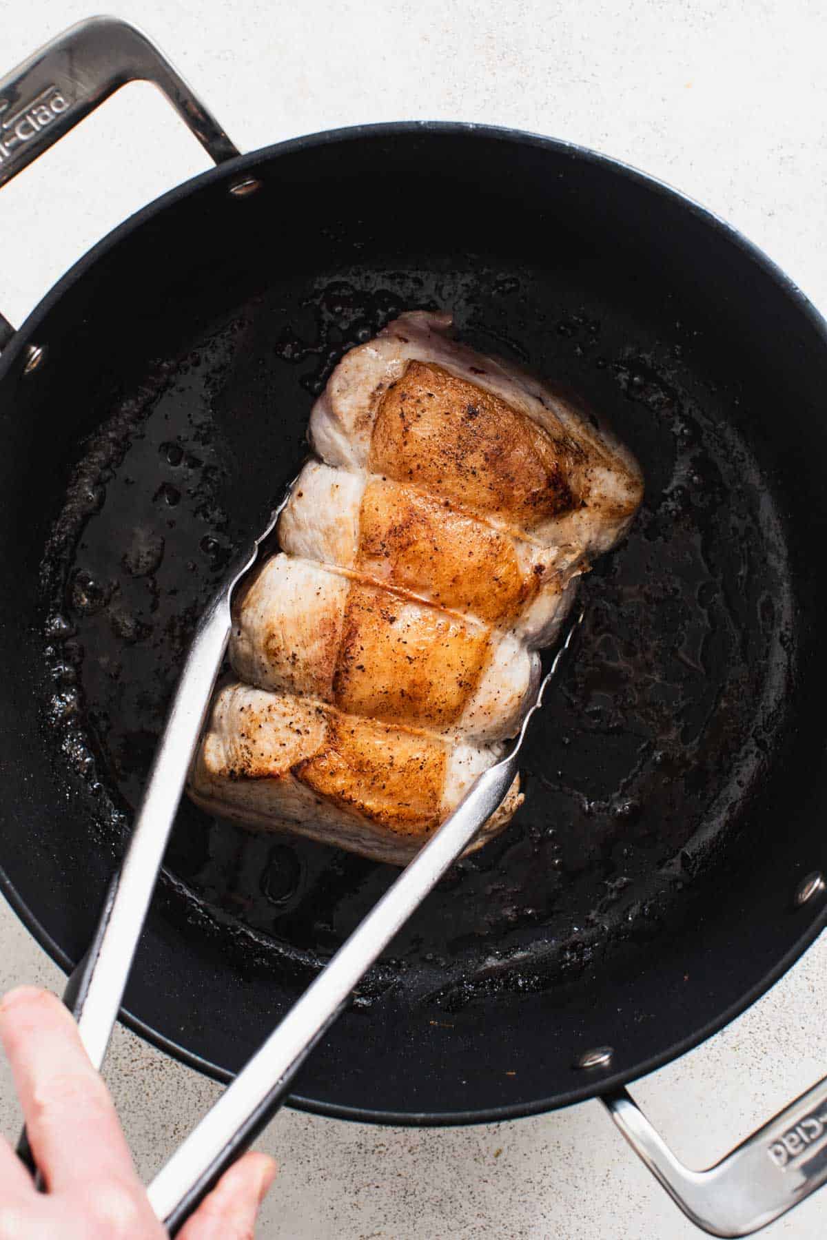 Searing a pork loin roast in a dutch oven pan till golden brown.