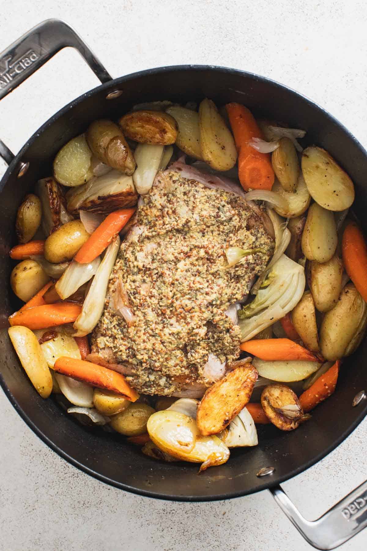 Adding dijon sauce on top of a pork loin roast in a dutch oven with vegetables.