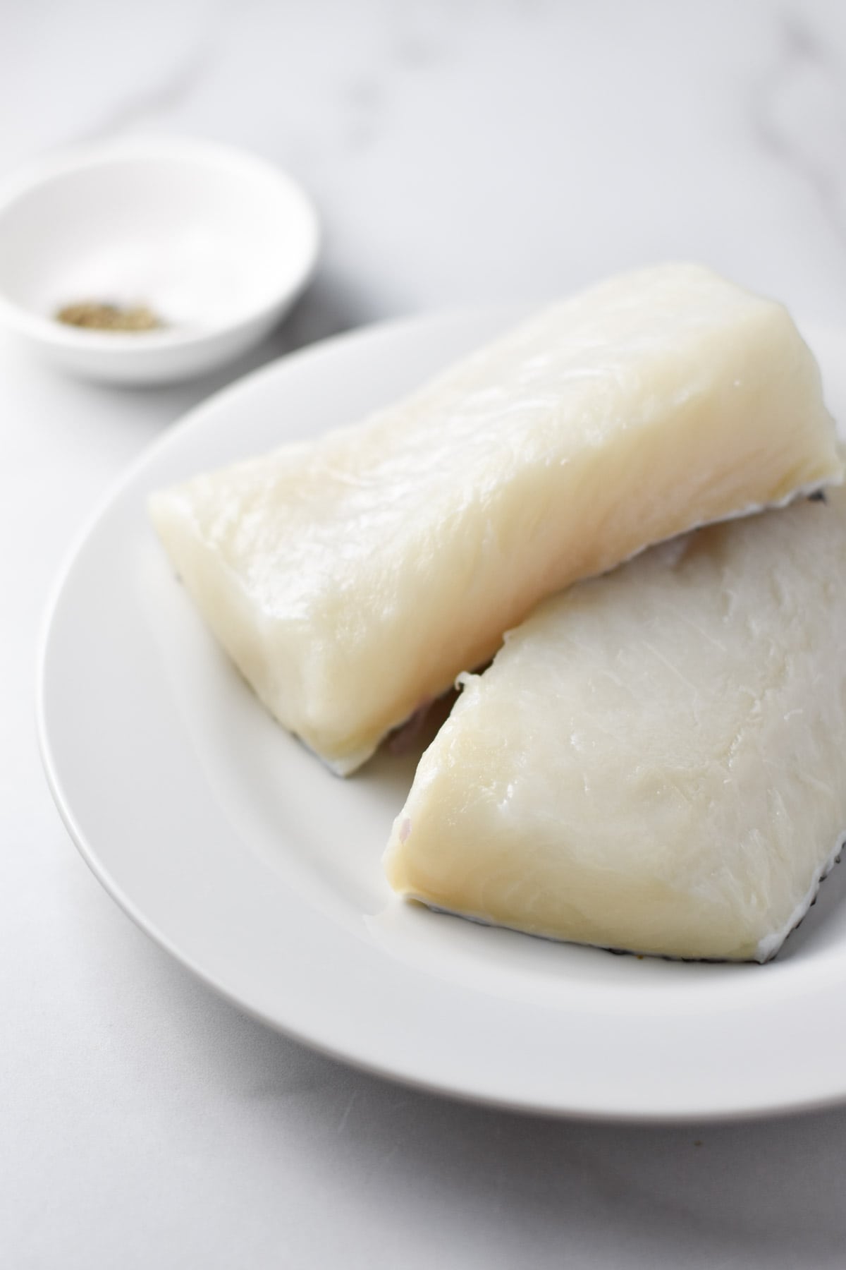 Uncooked Chilean sea bass fillets on a white plate.