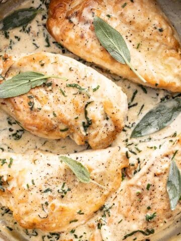 Four chicken breasts topped with sage in a creamy sauce.