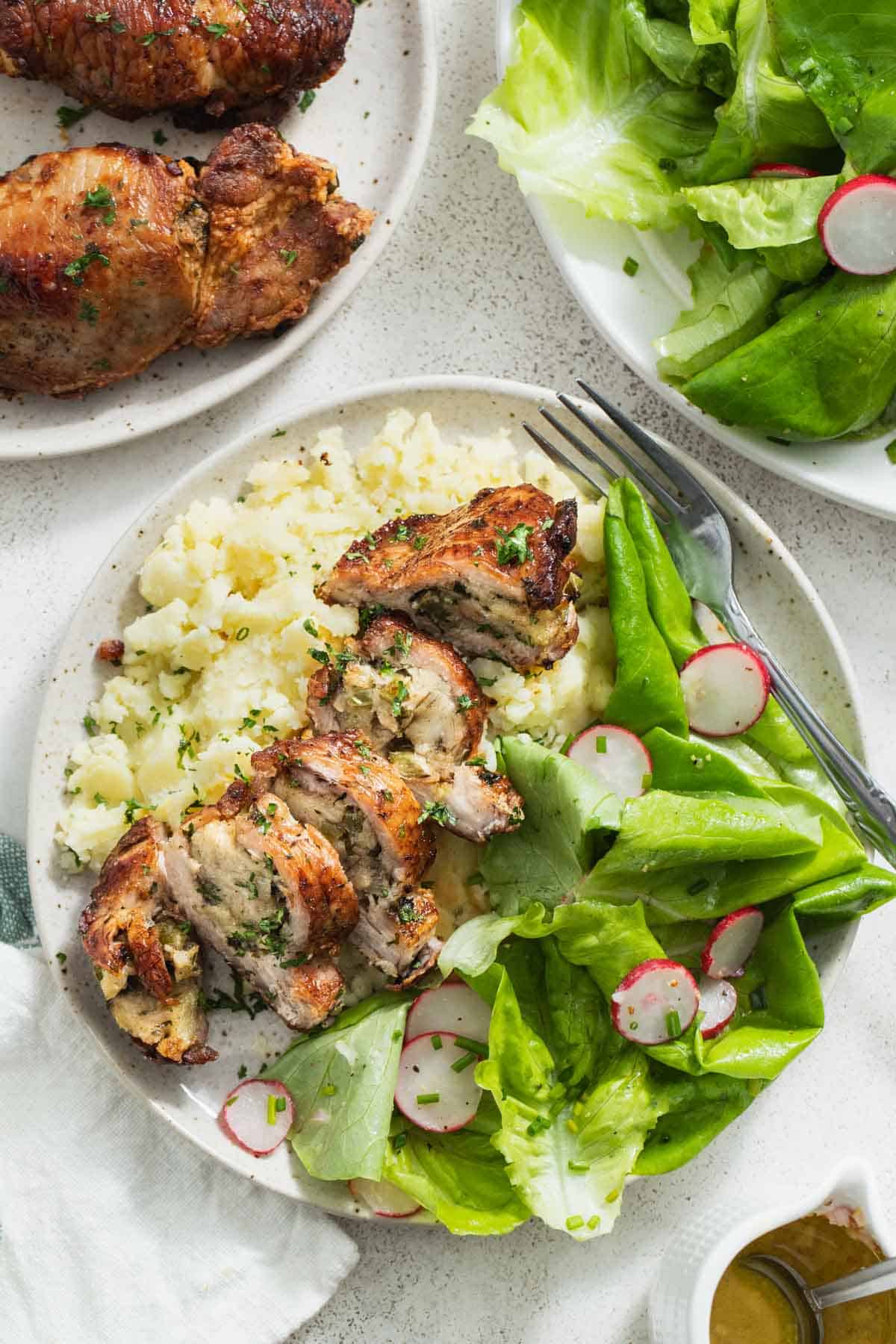 Stuffed pork chops sliced on a plate on top of mashed potatoes and a green salad.