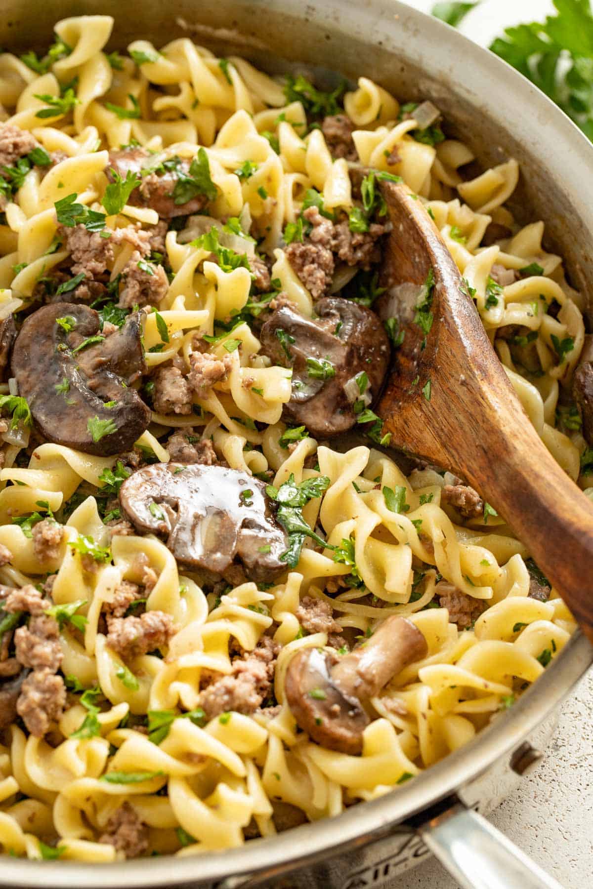 A pan filled with egg noodles and beef stroganoff with parsley.