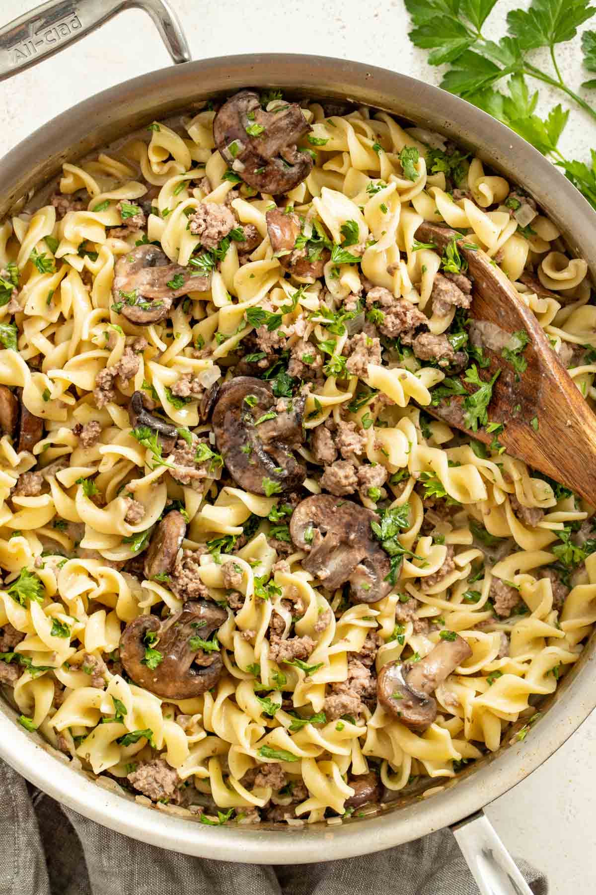Beef stroganoff noodles in a stainless steel all clad pan topped with parsley.