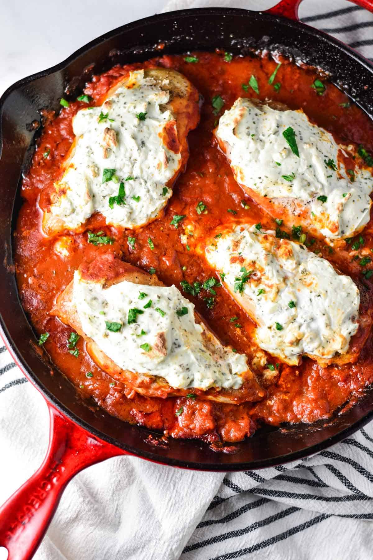 A large cast iron pan with 4 chicken breasts topped with a creamy ricotta mix. 