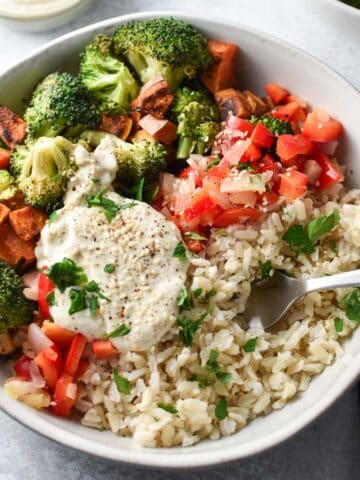 Broccoli, sweet potatoes, and rice all topped with chopped veggies and a sauce with a fork placed on the side of the bowl.