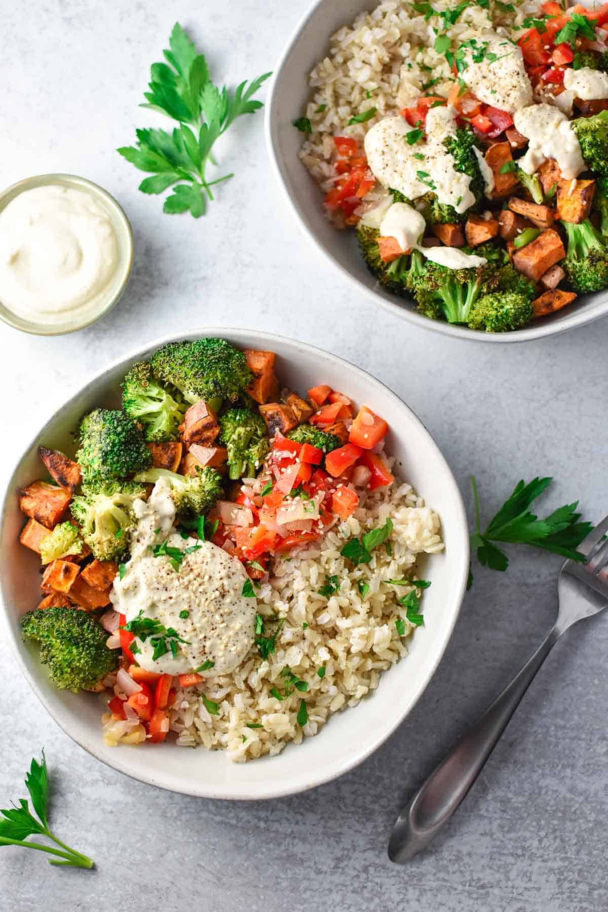 Two sweet potato bowls filled with rice, broccoli, and veggies next to a small bowl of creamy tahini sauce.