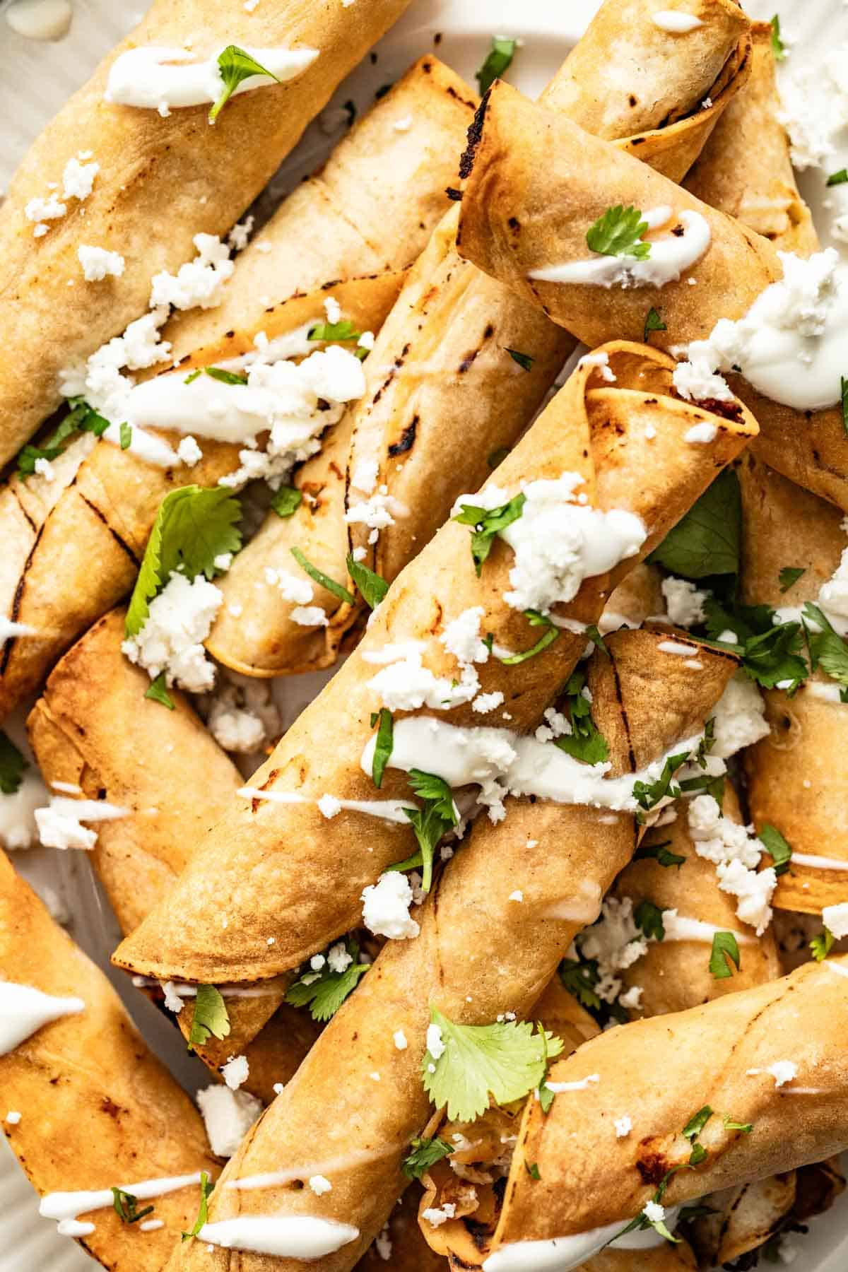 A stack of chicken taquitos topped with queso fresco.