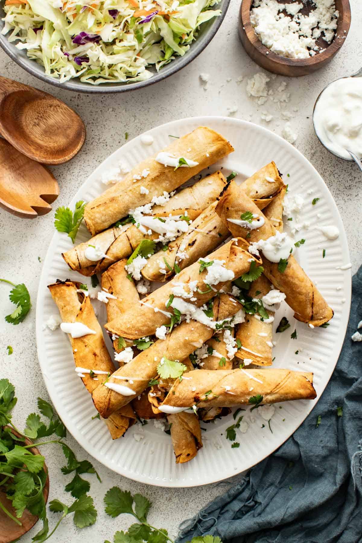 Chicken taquitos stacked on a white plate, drizzled with sour cream sauce and cilantro.