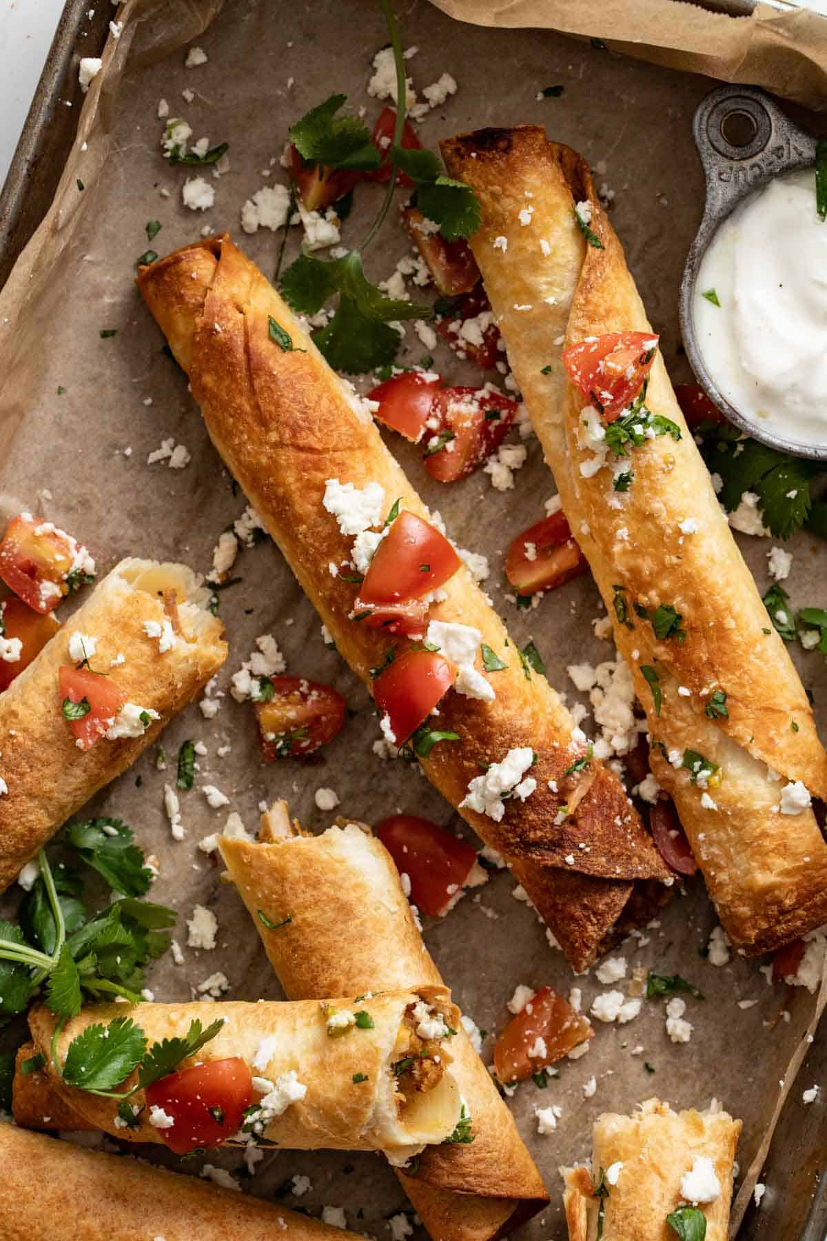 Chicken flautas with cheese and tomatoes on a baking sheet.
