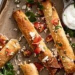 Baked chicken flautas with crumbled cheese, tomatoes, and cilantro on a baking sheet.