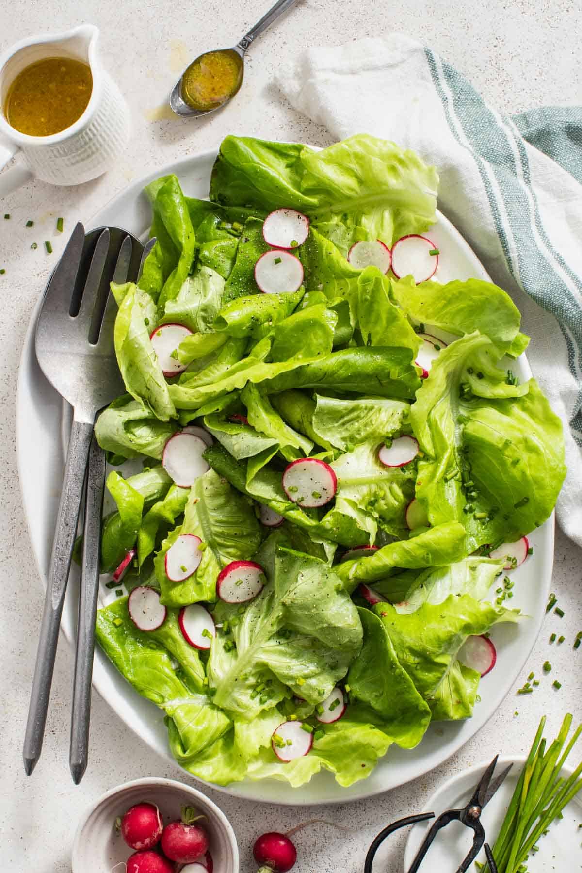 A bibb lettuce salad with two large serving utensils next to it.