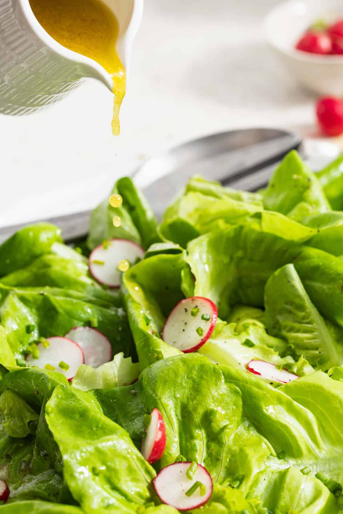 Pouring dijon dressing on a side salad.