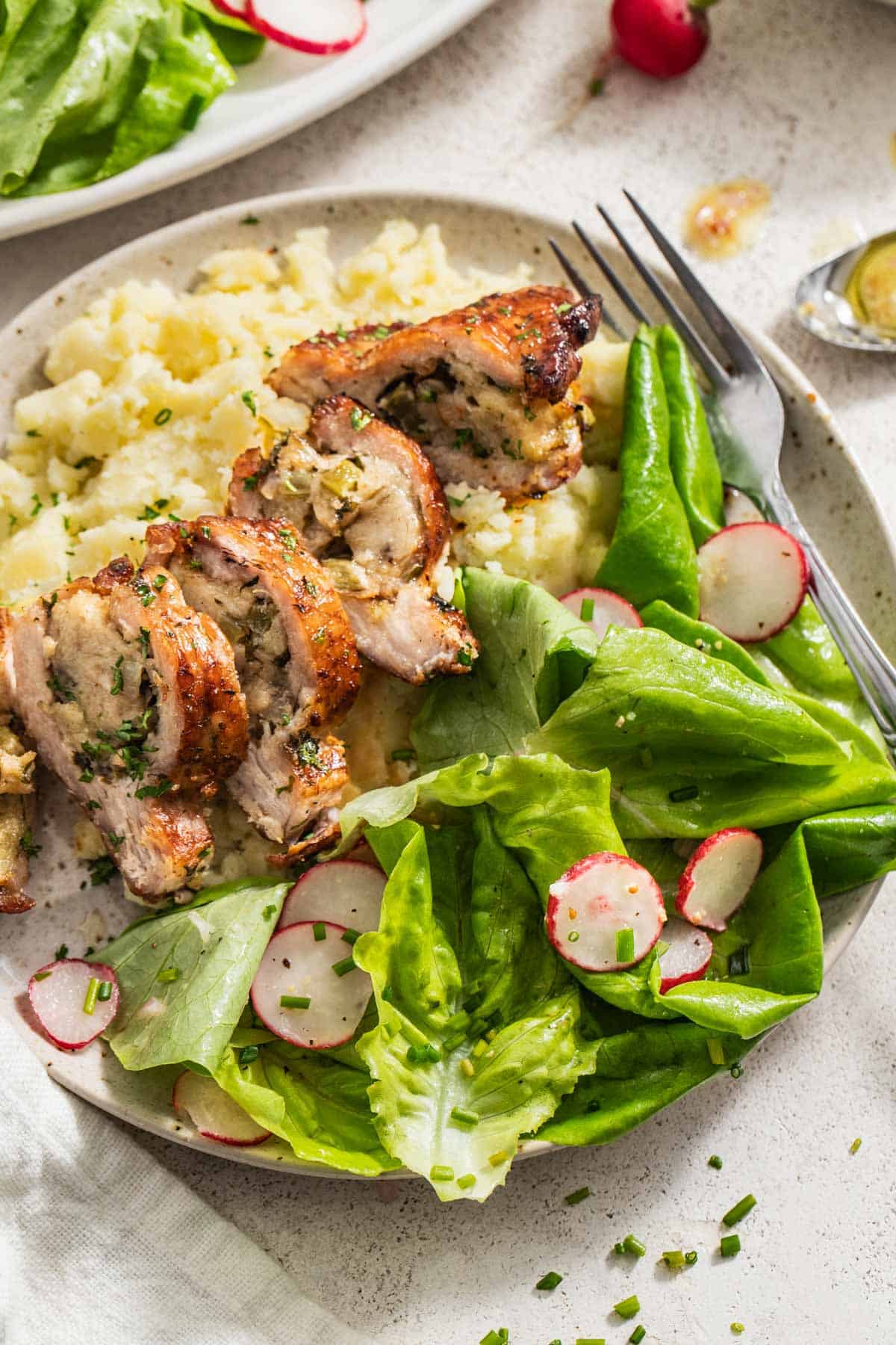 A butter lettuce side salad next to stuffed pork chops and mashed potatoes.