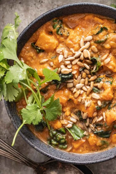 A bowl of sweet potato soup topped with cilantro and roasted sunflower seeds.