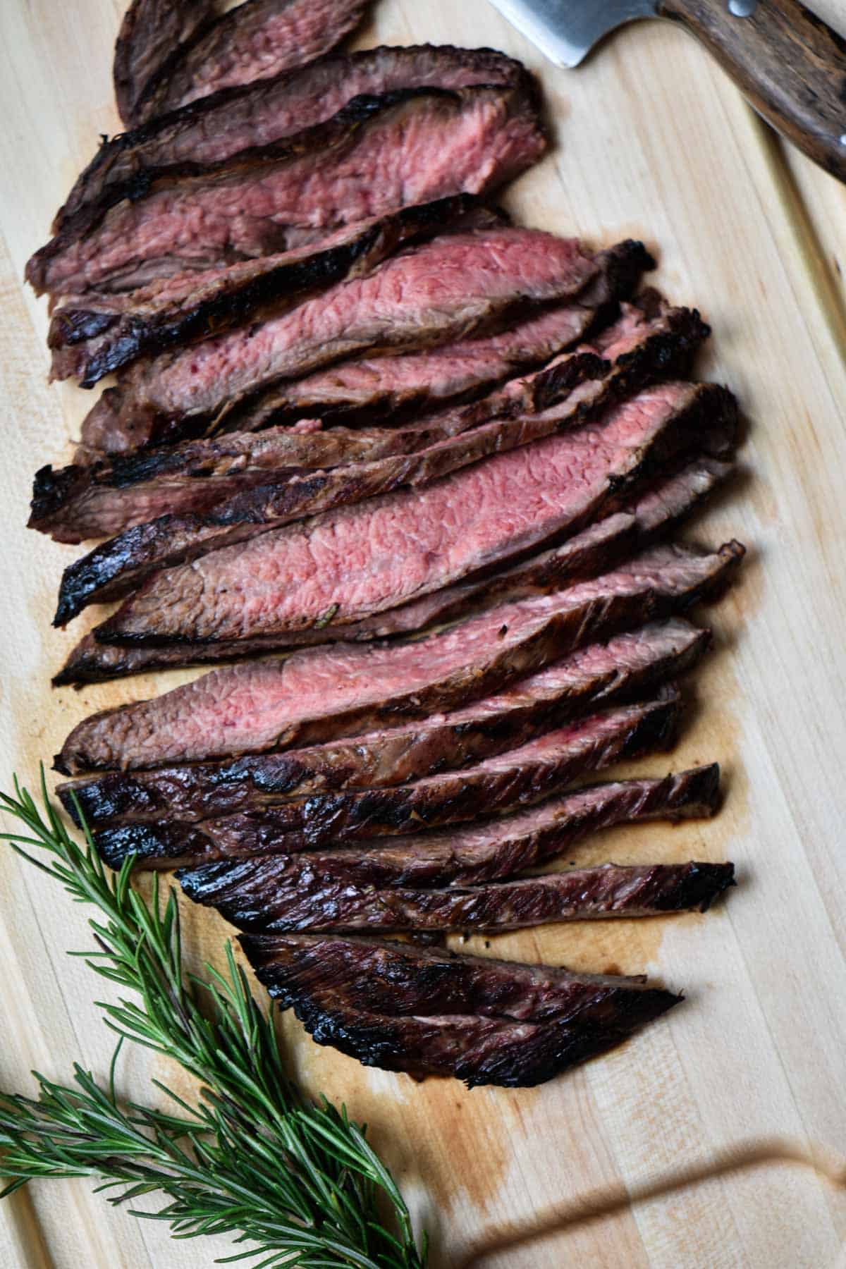 Marinated flank steak on a cutting board with rosemary.