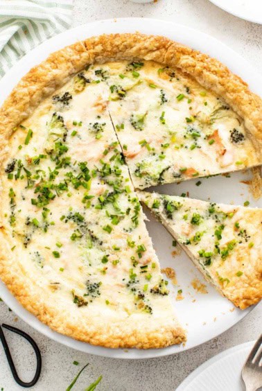 A slice being cut out of a whole salmon and broccoli quiche.