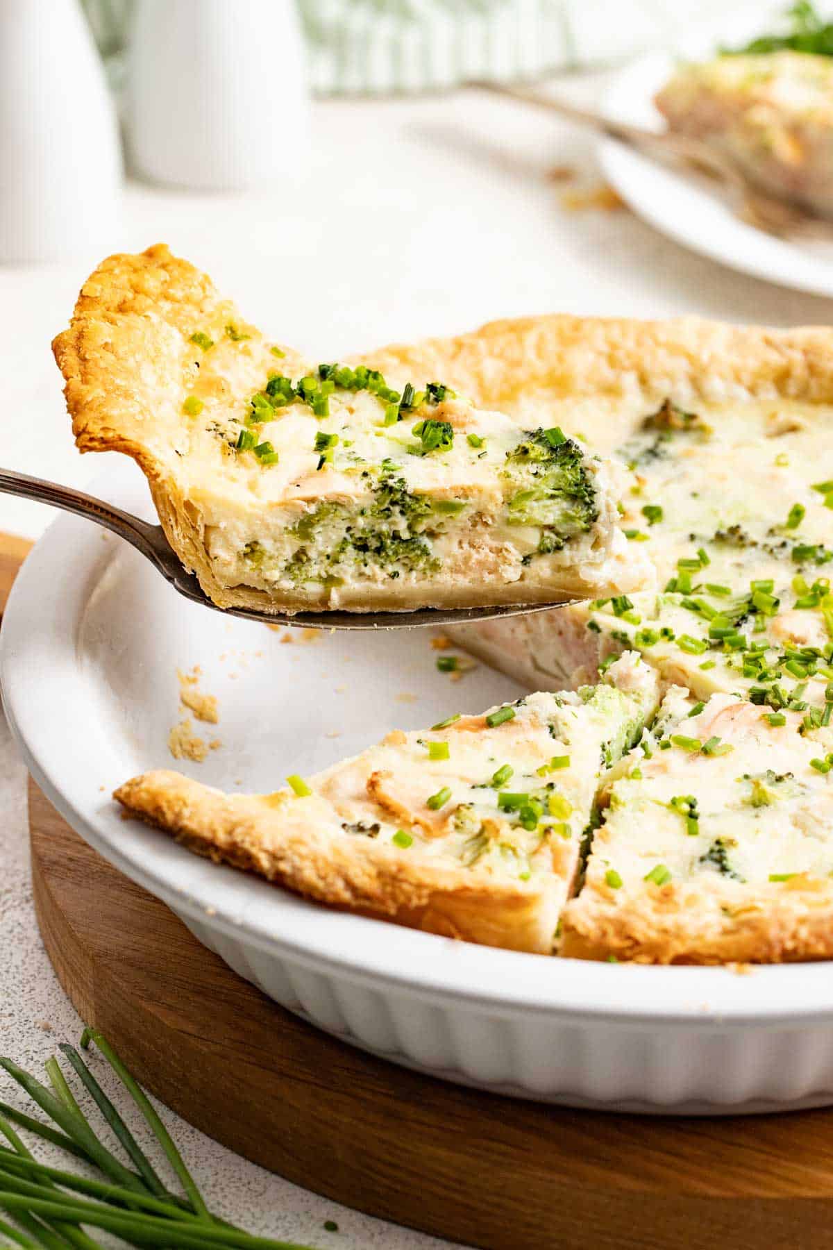 A serving utensil lifting a slice of broccoli quiche out of the pie plate.