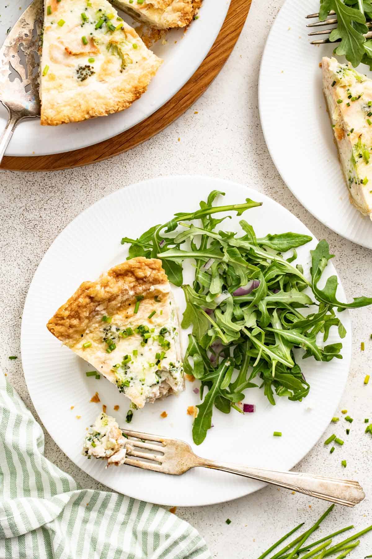 An overhead photo of a slice of quiche with salmon and arugula salad.
