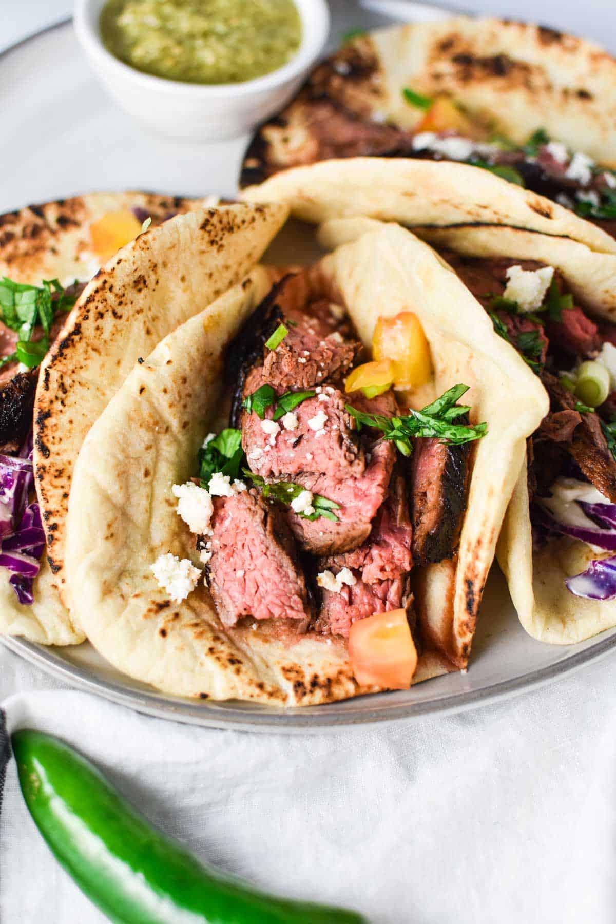 A flank steak taco topped with queso fresco and tomatoes.