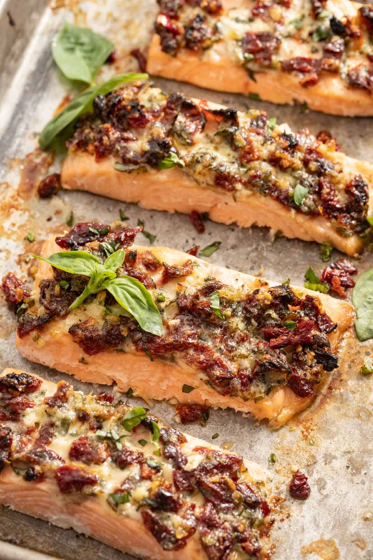 4 salmon fillets topped with a Mediterranean tomato mixture on a sheet pan with basil.