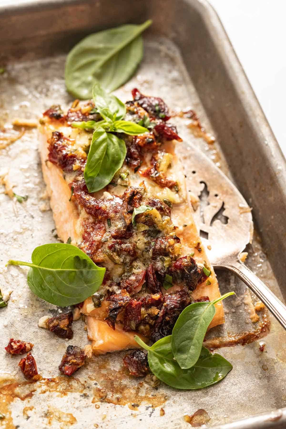 A sheet pan with a slice of salmon topped with basil and sun-dried tomatoes.