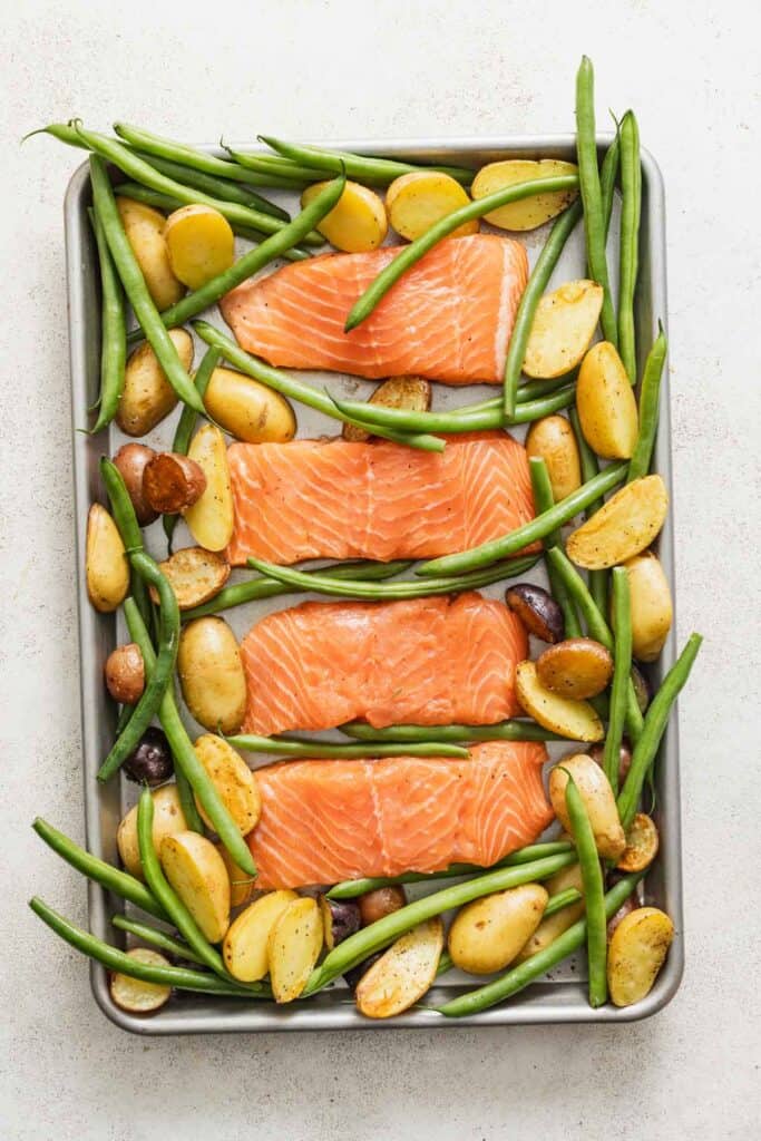Salmon, green beans, and potatoes on a sheet pan before baking.