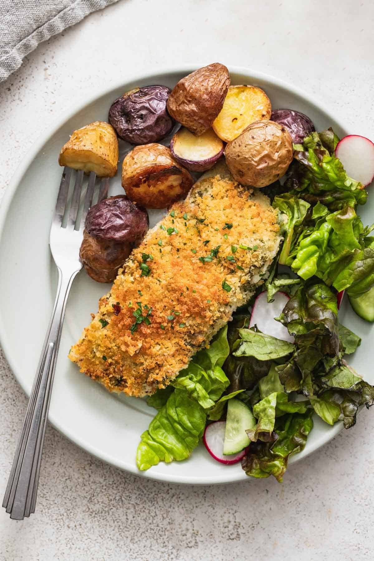 Panko crusted halibut on a plate with multi-colored roasted potatoes and a green salad.