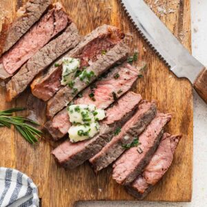 Air fryer New York strip steak sliced on a cutting board and topped with a melted compound butter.